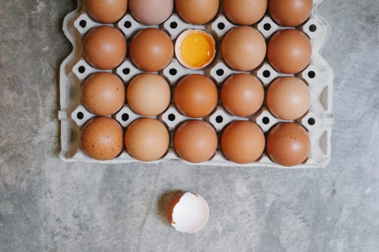 Caixa com vários ovos marrons com um ovo com casca quebrada.